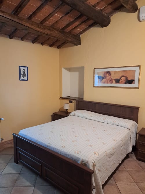Rustic bedroom at Corte Pincione B&B in Montecarlo with dark wood bed, beamed ceiling, and yellow walls