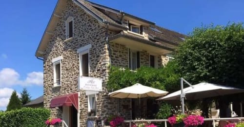 Hôtel Saint Roch, bâtiment en pierre avec terrasse, parasols et fleurs roses à Saint Ybard, France