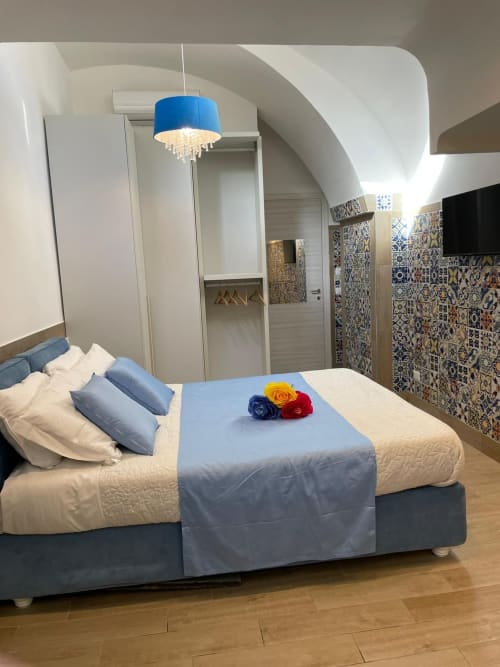 Camera moderna della San Nicola Suite a Sorrento con lampada a sospensione blu, parete in piastrelle decorate e rose sul letto