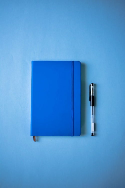 Blue notebook with elastic band and pen on light blue background at Vila Alexandra hostel, Costa da Caparica