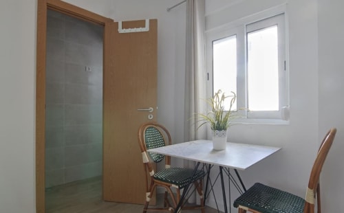 Modern hostel room at Vila Alexandra in Costa da Caparica with dining table, wicker chairs, and glass shower door