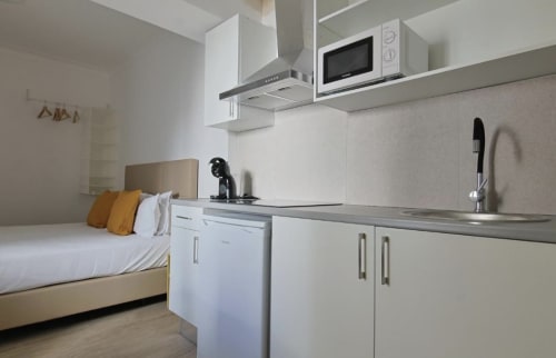 Modern studio apartment at Vila Alexandra hostel in Costa da Caparica with bed, kitchenette, and white appliances
