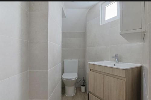 Modern bathroom at Vila Alexandra hostel in Costa da Caparica with toilet, wooden vanity, white sink, and tiled walls