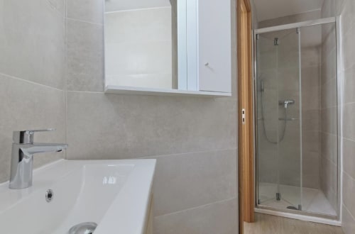Modern bathroom in Room B1 at Vila Alexandra hostel, Costa da Caparica, featuring white sink, mirror cabinet, and glass