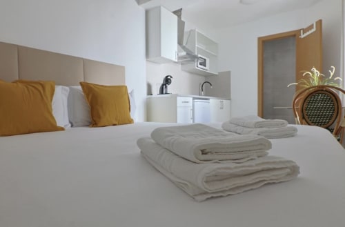 Modern hostel room at Vila Alexandra in Costa da Caparica with bed, kitchenette, and gold accent pillows
