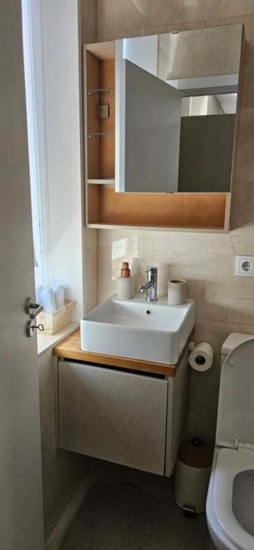 Banheiro moderno do apartamento Casa Da Avó Ilda com pia branca quadrada, gabinete de madeira, espelho e vaso sanitário