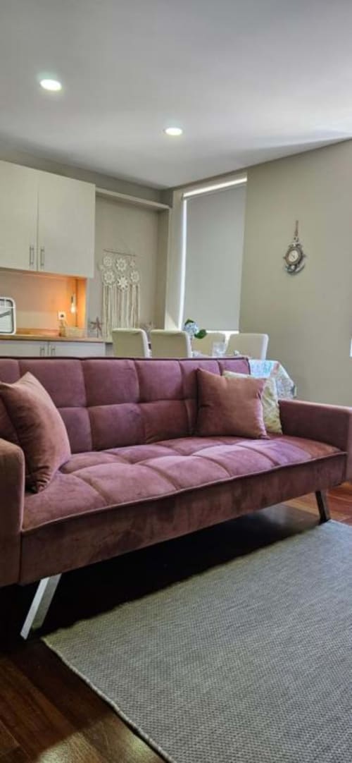 Sofisticada sala de estar de apartamento moderno com sofá roxo aconchegante, cozinha e vista para a cidade no alojamento de Matosinhos