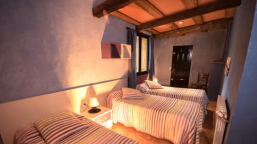 Cálida habitación en Can Gat Vell B&B en Girona con ropa de cama a rayas, vigas de madera e iluminación ambiental