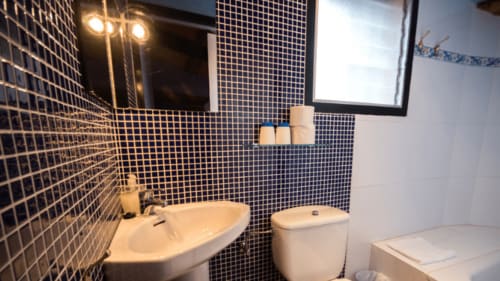 Baño moderno en el Can Gat Vell B&B en Girona con azulejos azul marino, lavabo blanco, inodoro y espejo iluminado