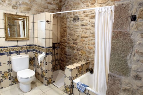 Baño rústico en Can Gat Vell B&B en Girona con paredes de piedra, azulejos decorativos y cabina de ducha.