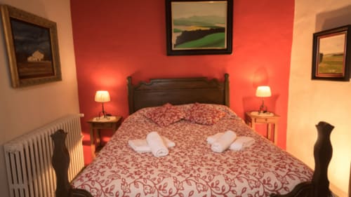 Acogedora habitación en Can Gat Vell B&B en Girona con pared roja, cama de madera oscura y cómodas zapatillas