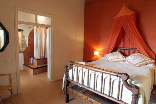 Dormitorio rústico en Can Gat Vell B&B en Girona con cama de hierro forjado ornamentada, dosel rojo y paredes de terracota