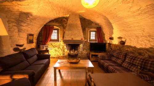 Salón de piedra con bóvedas de Can Gat Vell B&B en Girona, con chimenea, sofás e iluminación cálida
