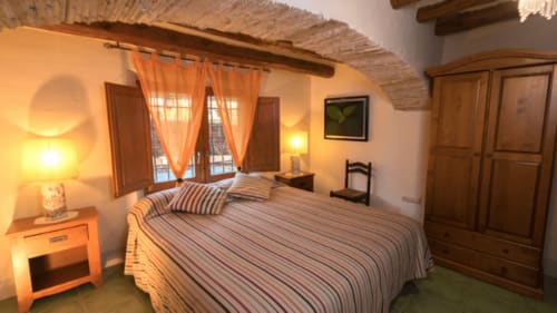 Acogedora habitación en el B&B Can Gat Vell de Girona con vigas de madera, ropa de cama a rayas e iluminación cálida