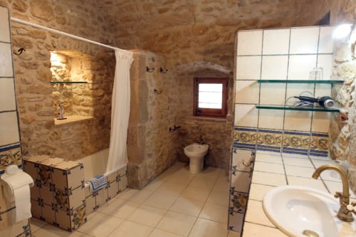 Amplio baño rústico en Can Gat Vell B&B en Girona, con paredes de piedra, azulejos decorativos, ducha y lavabo pedestal