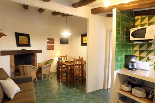 Sala de estar abierta del B&B Can Gat Vell en Girona con chimenea, mesa de comedor y cocina con azulejos verdes