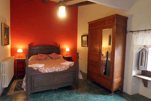 Habitación en Can Gat Vell B&B en Girona con paredes rojas, cama de madera oscura, armario antiguo y suelo de baldosas