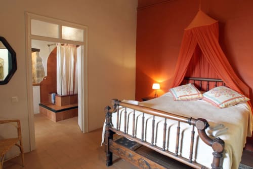 Dormitorio romántico en Can Gat Vell B&B en Girona con cama de hierro forjado, dosel rojo y paredes de terracota cálida