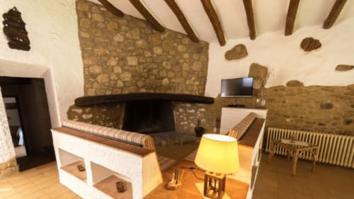 Dormitorio rústico Can Gat Vell en Girona con chimenea, vigas vistas, muros de piedra y lámpara de mesa amarilla