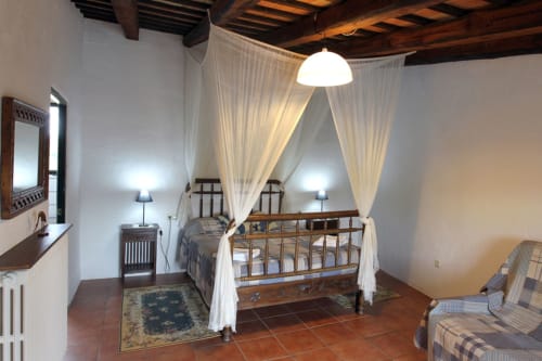 Elegante cama con dosel y cortinas blancas en una habitación rústica de Can Gat Vell, un alojamiento boutique en Girona, Cataluña