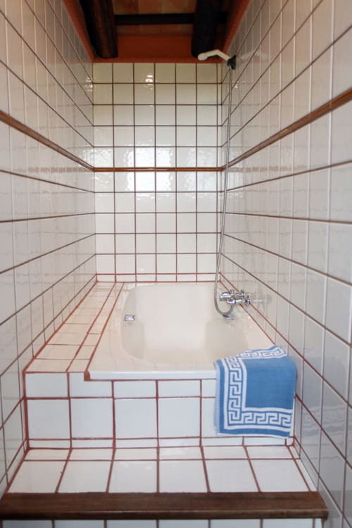 Baño con azulejos blancos, patrón de cuadrícula roja, bañera y toalla azul en el hotel boutique Can Gat Vell en Girona, Cataluña