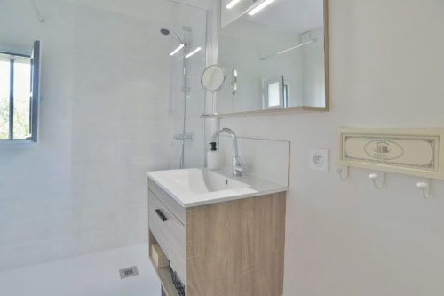 Salle de bain moderne de la villa Maison Grand Large avec meuble-lavabo en bois, lavabo blanc, grand miroir et douche vitrée