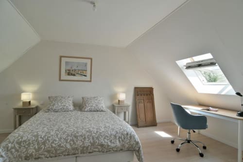 Chambre lumineuse sous les combles de la villa Maison Grand Large avec puits de lumière, literie à motifs, mobilier en bois et vue sur le jardin