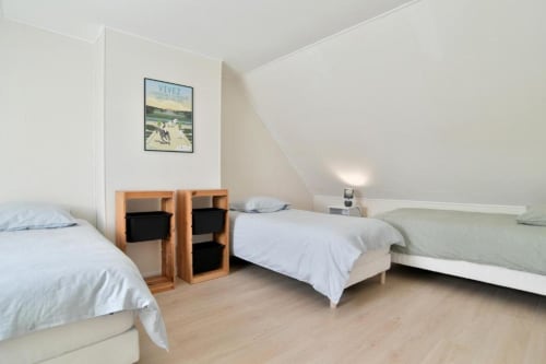 Chambre à plusieurs lits de la villa Maison Grand Large avec literie blanche, rangements en bois et vue sur le jardin à Saint-Cast-le-Guildo