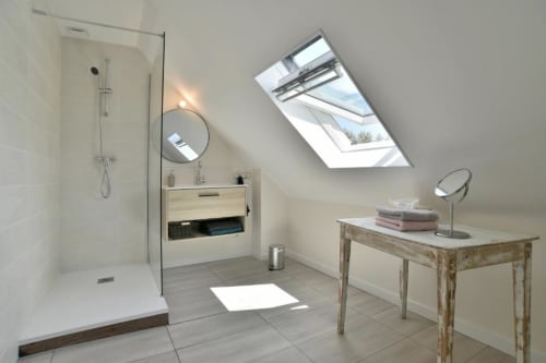 Salle de bain mansardée moderne à la villa Maison Grand Large avec lucarne, douche italienne, meuble-lavabo en bois et lumière naturelle
