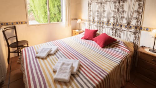 Cama de rayas coloridas con almohadas rojas en una habitación luminosa del alojamiento Can Gat Vell B&B, Girona, Cataluña