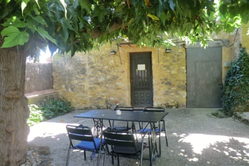 Zona de estar en la terraza de Can Gat Vell, Girona con mesas y sillas bajo un edificio de piedra cubierto de enredaderas