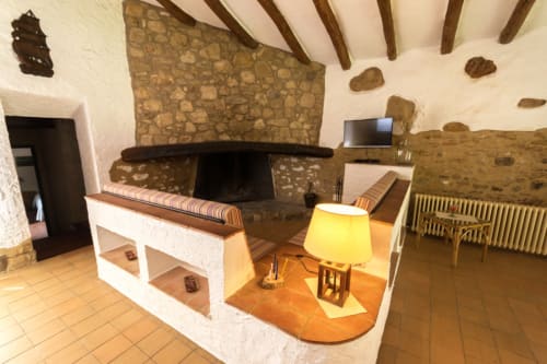 Sala de estar rústica de granja con chimenea, vigas de madera y lámpara amarilla en Can Gat Vell en Girona
