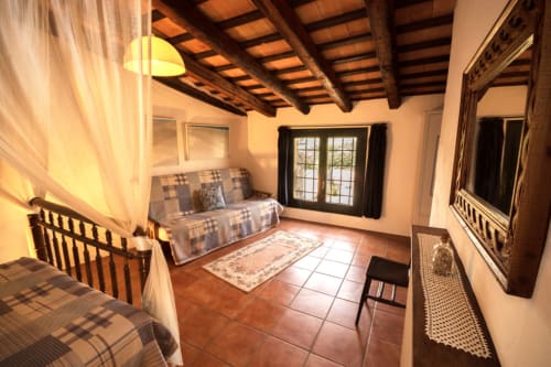 Dormitorio rústico con vigas de madera, baldosas de terracota, cama con dosel y puertas al jardín en la masía Can Gat Vell