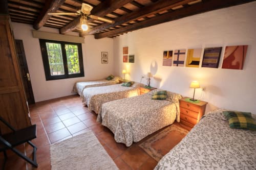 Dormitorio luminoso en casa de campo del siglo XVIII en Can Gat Vell con cuatro camas, vigas de madera vista, suelo de baldosas de terracota, jardín