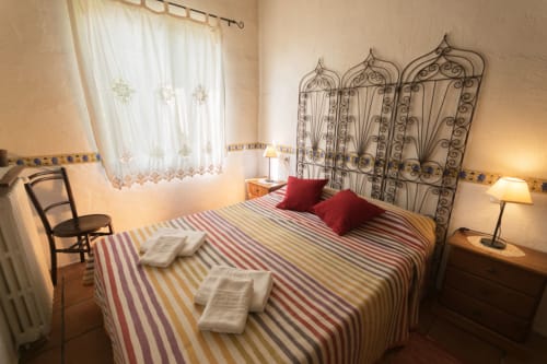 Cómodo dormitorio en una casa de campo del siglo XVIII en Girona con ropa de cama a rayas, cabecero de hierro forjado y vistas al jardín