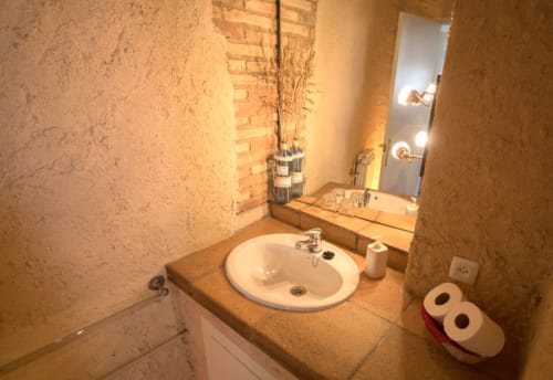 Baño rústico con lavamanos redondo, pared de ladrillo y espejo en la casa rural Can Gat Vell, Girona