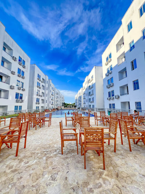 Área de piscina del resort con tumbonas de madera, edificios blancos de apartamentos y patio arenoso en Olamar Living en Coveñas,