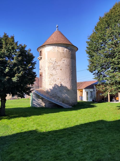 Historic cylindrical dovecote tower with conical roof at Manoir Saint Joseph in Sens, France, surrounded by green lawn and