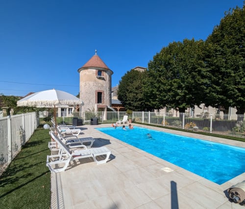 Swimming pool with lounge chairs at Manoir Saint Joseph hotel in Sens, France, with historic tower building