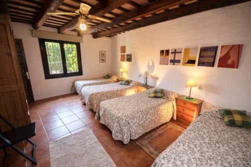 Dormitorio espacioso con cuatro camas, vigas de madera rústica, suelo de baldosa de barro y vistas al jardín