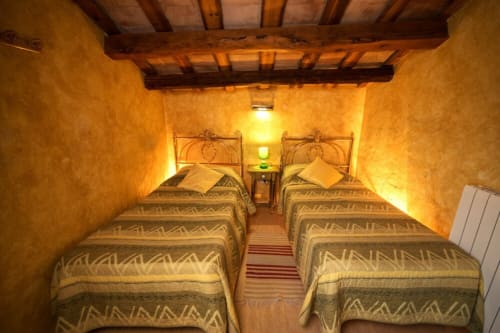 Acogedor dormitorio doble de la masía Can Gat Vell, Girona, con iluminación cálida y vigas rústicas