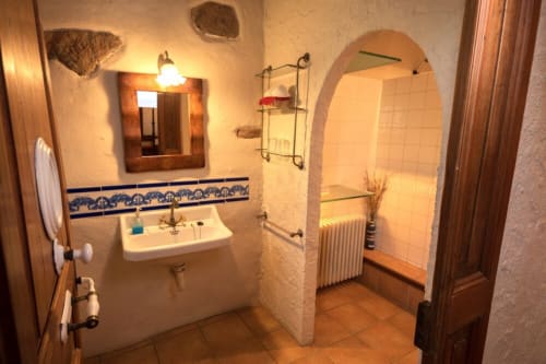Baño rústico con lavabo blanco, azulejos azules decorativos, nicho de ducha abovedado e iluminación cálida en la masía Can Gat Vell