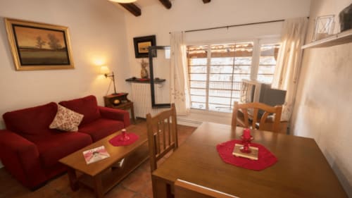 Acogedor salón del alojamiento Can Gat Vell en Girona con sofá rojo, mesa de comedor de madera y puertas hacia el balcón