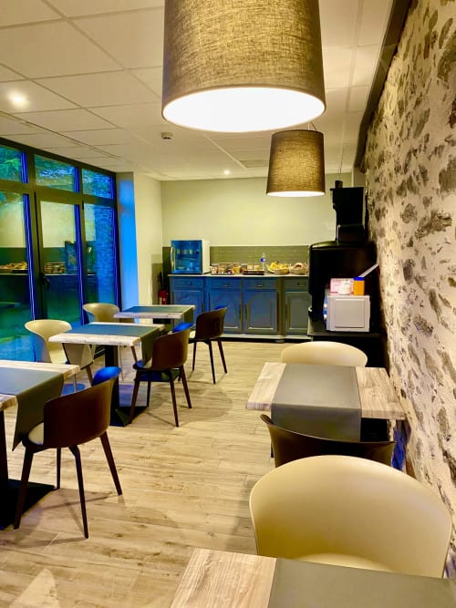 Élégant espace lounge de l'Hôtel Saint Roch avec sièges, tables, luminaires suspendus et cuisinette à Saint Ybard