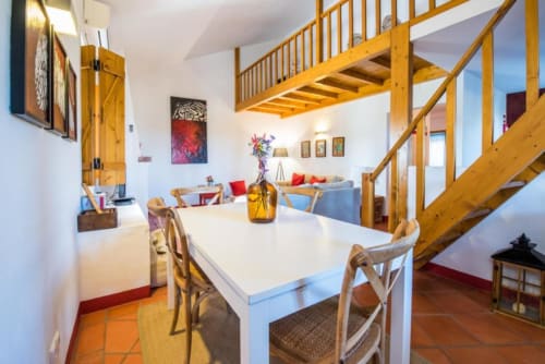 Espaço integrado e luminoso de sala de jantar e estar na villa Juromenha com escadas de madeira, mesa branca e móveis confortáveis.