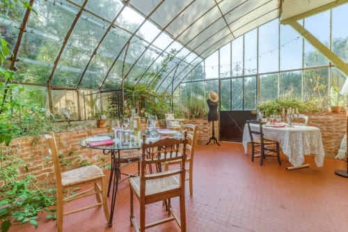 Glass greenhouse dining room with wooden tables at Baccara Lodge in Arengosse, France, featuring lush plants and countryside