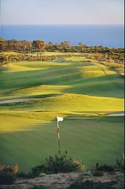 Buraco de golfe com bandeira branca com vista para paisagem verde e oceano em Casas de Juromenha, Portugal