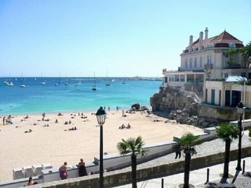 Waterfront de Cascais com praia arenosa, água cristalina, barcos e edifício histórico nas Casas de Juromenha