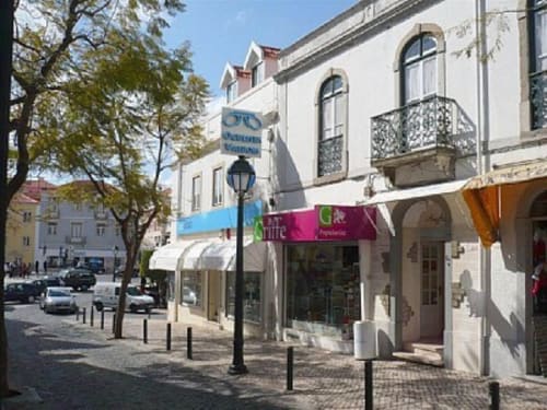 Loja Casas de Juromenha em Cascais, Portugal com fachada de edifício branco, sinalização azul e comércios no nível da rua