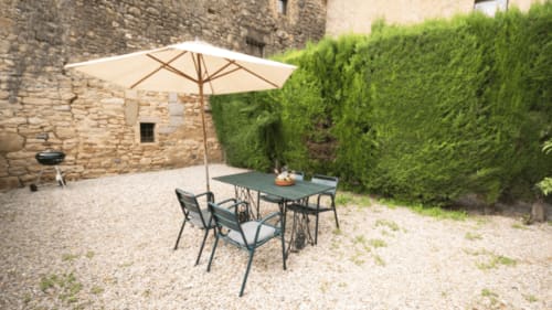 Patio exterior del Can Gat Vell B&B en Girona con mesa de comedor, sillas, sombrilla crema y frondosos setos.